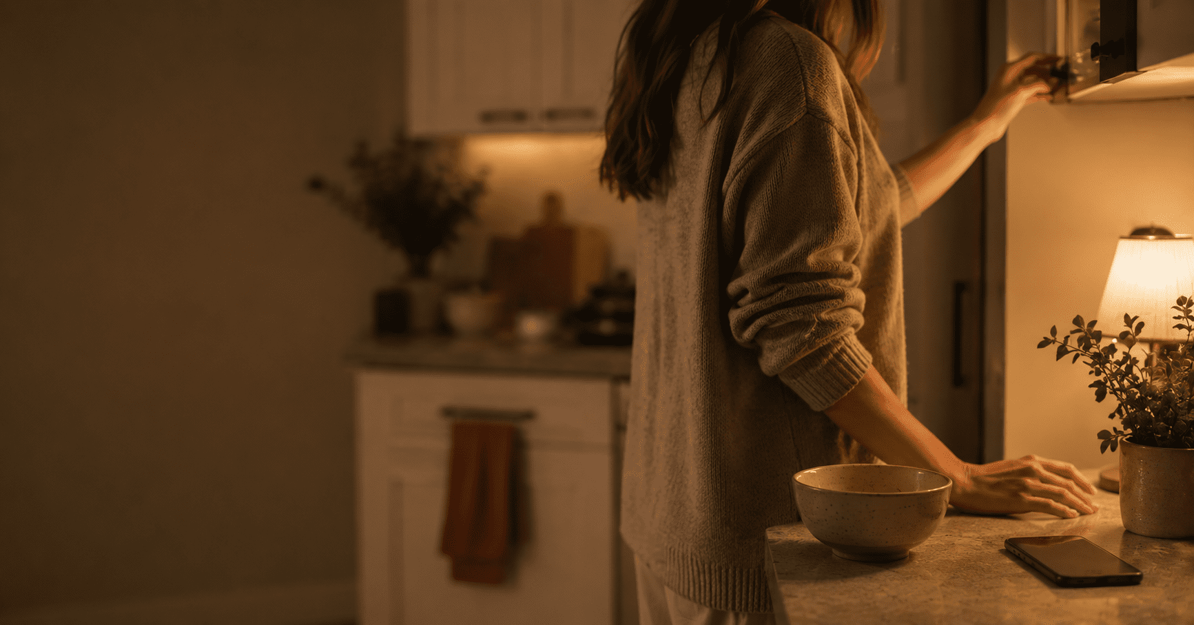 Person reaching into a softly lit kitchen at night out of boredom, not hunger, illustrating how to stop snacking so much