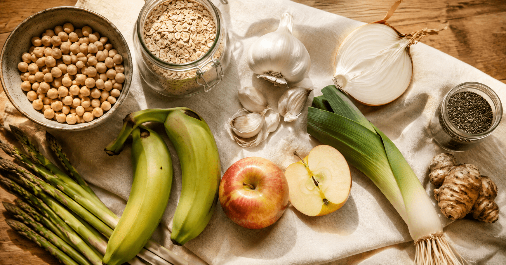 Prebiotic Foods That Feed Beneficial Gut Bacteria and Reduce Cravings (The Part Nobody Talks About) Prebiotic foods that feed gut bacteria flat lay including chickpeas oats garlic onions chia seeds asparagus green banana apple and Jerusalem artichoke