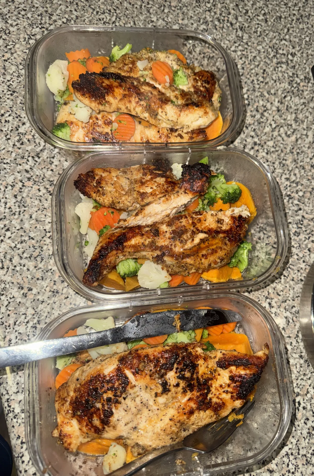 Three glass meal prep containers with seasoned chicken breast and mixed vegetables